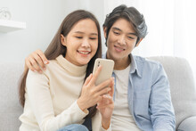 Happy Couple Love At Home,beautiful Two Asian Young Spending Good Time Together,bonding To Each Other And Smiling Romantic On Sofa In Living Room While Man Embrace Woman Using Smartphone, Mobile Phone