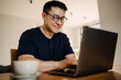 Adult smiling asian man in glasses studying with laptop