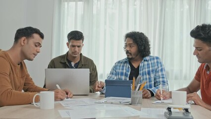 Wall Mural - medium slowmo of four young creative male indian entrepreneurs discussing business project at table 