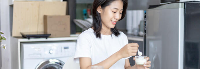 Half-Japanese woman eats yoghurt with cereal for breakfast in room, Healthy food and digestive system maintenance, The most popular and easy to eat breakfast food.