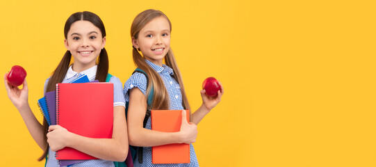 Poster - School girls friends. Happy pupils with books hold vitamin organic apples yellow background, school breakfast. Banner of school girl student. Schoolgirl pupil portrait with copy space.