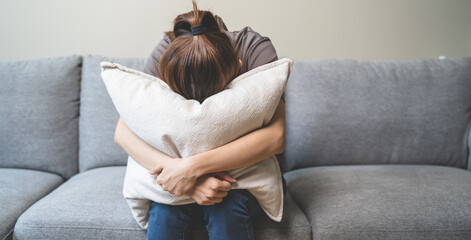 Wall Mural - Unhappy anxiety young Asian woman covering her face with pillow on the cough in the living room at home.