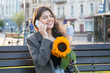 © puhimec - A young woman with a bouquet of sunflowers is talking on the phone at sunset.