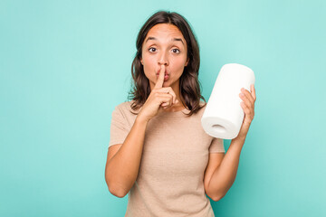 Wall Mural - Young hispanic woman holding kitchen roll isolated on blue background keeping a secret or asking for silence.