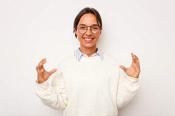 Wall Mural - Young hispanic woman isolated on white background holding something with palms, offering to camera.