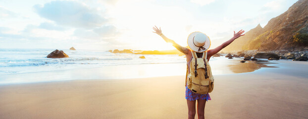 Happy female traveller with backpack and hands up enjoying sunset on the beach - Delightful woman raising arms outside - Journey lifestyle and summer vacations concept