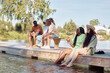 © Seventyfour - Diverse group of young people relaxing on pier by water in Summer setting, copy space