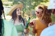 © Seventyfour - Portrait of two smiling young women clinking beer bottles outdoors while enjoying party with friends in Summer