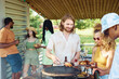 © Seventyfour - Waist up portrait of smiling man grilling meat outdoors during Summer barbeque party with friends