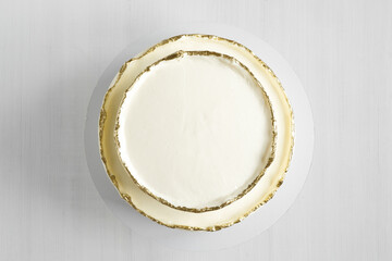 Wall Mural - Cake with white cream, decorated with gold confectionery sprinkles on a white background. Two-tiered white wedding cake. Top view.