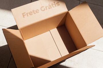 Open cardboard box with sunlight written on frete gratis. Putting present inside the empty cardboard box. Box concept. Unboxing concept.