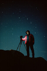 Man is taking photos of night sky with camera on tripod