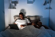 © Ezequiel Giménez/Stocksy - Black male watching video near sleeping girlfriend