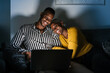 © Ezequiel Giménez/Stocksy - Cheerful black couple chilling on laptop at night