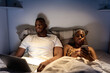 © Ezequiel Giménez/Stocksy - African American couple using gadgets during bed time