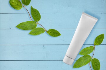 Wall Mural - White Cream tube and branches with young small leaves. Cosmetic skincare product blank plastic package. White bottle of unbranded lotion, balsam, toothpaste mockup