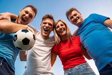 Group of ecstatic fans hugging together , view from bellow, sky background . Face paint on, fun mode on!