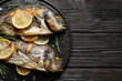 Delicious roasted fish with lemon on black wooden table, top view. Space for text