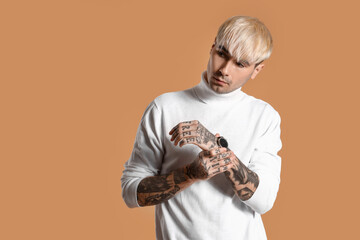 Young tattooed man in white sweater on brown background