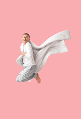 Young man with blanket jumping on pink background