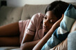 © David Prado/Stocksy - Young black woman worried lying on sofa at home