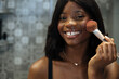 © David Prado/Stocksy - Smiling black woman applying makeup