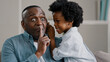 © Yuliia - Little african american daughter whispering secret adult dad in ear telling gossip surprised dad carefully listens confidential information making gesture silence secret puts index finger to mouth