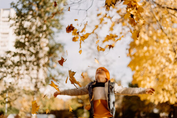 Kid having fun in autumn park with fallen leaves, throwing up leaf. Child boy outdoors playing with maple leaves