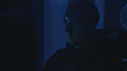 Portrait of dangerous hacker programmer working on computer scheming cyber attack on server in the office at night. Young male virtual spy hacking some software at night in the dark room