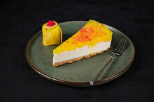 A Piece Of Mango Cheesecake With Mascarpone Cream Cheese Filling, Garnished With Fresh Mango, Served On A Plate With A Dessert Fork, Dark Background