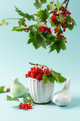 Wall Mural - Bowl with red currant berries, ceramic birds and branches with leaves and redcurrants on blue background. Summer composition, still life.