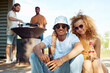 © Seventyfour - Portrait of young couple looking at camera while enjoying barbeque party with friends outdoors and holding beer bottles