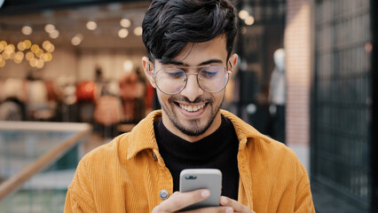 Close-up happy indian guy laughs watching funny video on smartphone looking at phone screen browsing web page on social network young man typing sms on dating site remote chat using virtual service