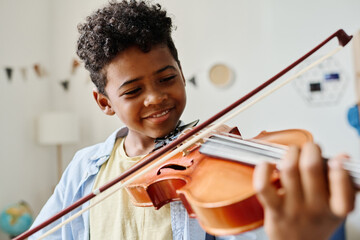 Smiling African boy playing violin at home during lesson