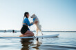 Leinwandbild Motiv Happy Young Woman with Locs Hugging with Her Dog Japanese Spitz While Sitting on the Sup Board on the Lake