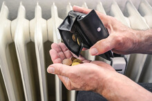 Hands Of A Man Pouring Out Few Coins From A Wallet In Front Of An Old Heater, Suffering From Rising Energy Costs, Copy Space, Selected Focus