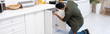 Young muslim man with screwdriver fixing cabinet under worktop in kitchen, banner