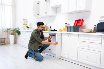 Wall Mural - Young arabian man with screwdriver fixing door of kitchen cabinet