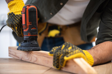 Wall Mural - Cropped view of carpenter sanding wooden plank with tool at home