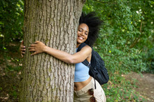 Young Woman Hiking In Forest, Hugging Tree