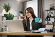 © sofiko14 - Attractive female freelancer with cup of coffee in casual outfit using modern laptop for work at home. Caucasian woman with dark hair sitting at table and typing on computer.