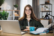 © sofiko14 - Pretty young caucasian woman with long dark hair sitting at table with modern laptop and touching glasses with hands. Concept of freelance and technology.
