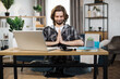© sofiko14 - Smiling caucasian man in casual wear sitting on workplace on yoga pose relaxing during break after working with modern laptop. Bearded male freelance meditating with closed eyes.