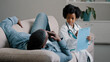 © Yuliia - Serious child pretends to be doctor in medical costume sitting writing symptoms on tablet father lies on couch complains of feeling unwell painful sensations african american dad playing with daughter
