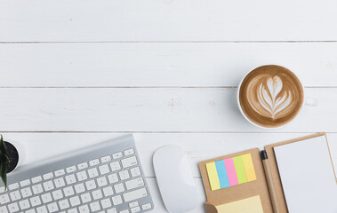 Top view table business of office with copy space. The desk in an office with equipment stationery business with keyboard, mouse, notebook, a pen, and mockup coffee on an old white wooden table.