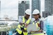 © amorn - Group of African American engineer worker working in sewer pipes area at construction site. Male engineer and woman engineer work with laptop computer for maintenance sewer pipes, water tank