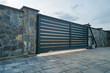 © bilanol - Wide automatic sliding gate with remote control installed in high stone fense wall. Security and protection concept