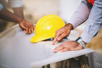 Close up construction engineers and foreman worker working together at construction site with building blueprints. Real estate work site project.