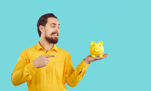 Saving Money And Making Profit. Man With Piggy Bank Offers To Make Favorable Financial Bank Offer Or Make Profitable Purchase. Joyful Man Pointing Finger At Piggy Bank In Hand On Light Blue Background