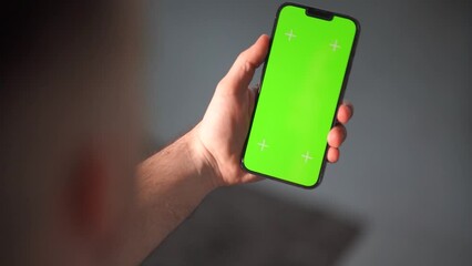 The man is using his phone in a vertical position. The green screen of the smartphone for chroma keying and tracking